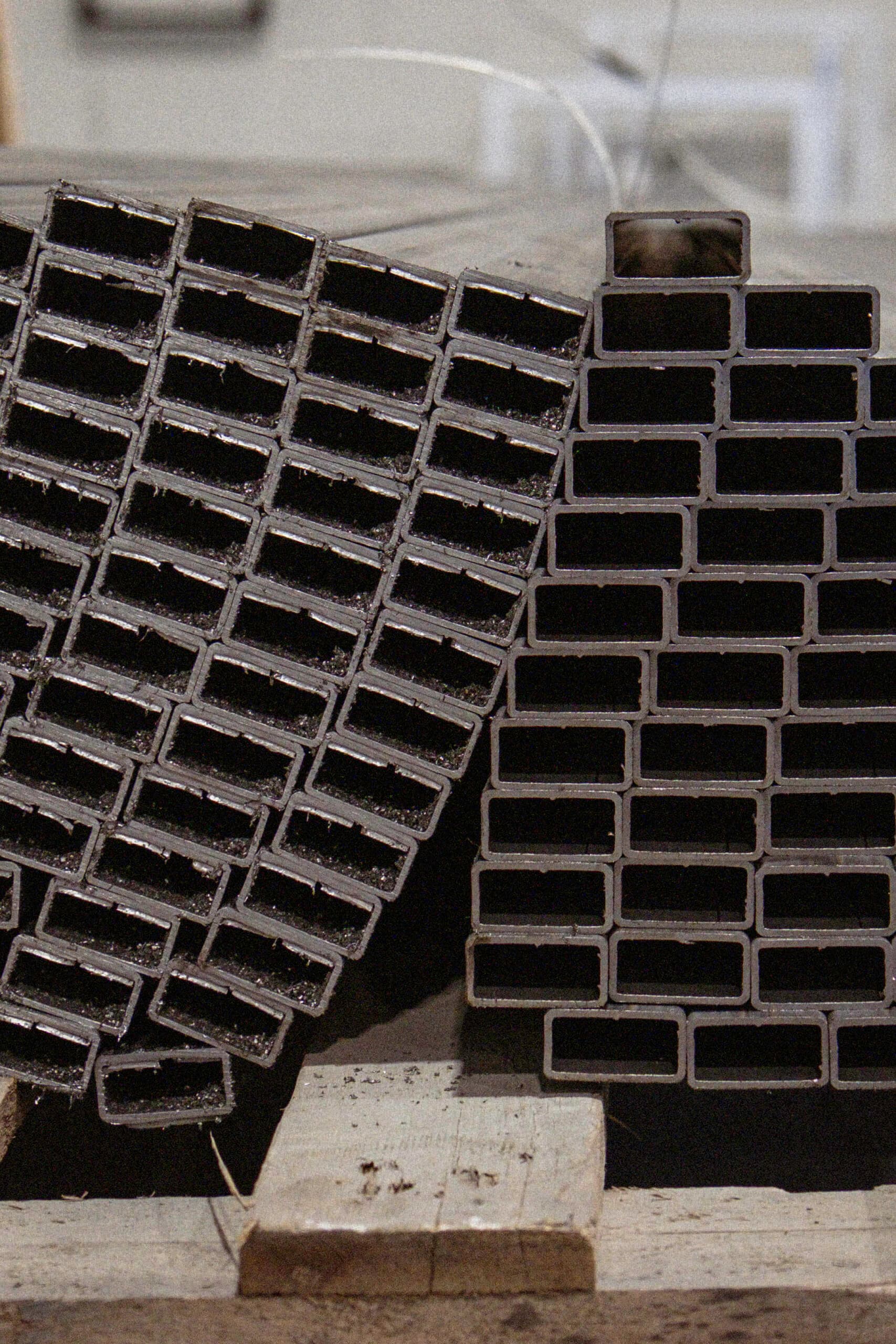 Stacks of rectangular hollow metal tubes arranged upright in a workshop, showing their open ends and rough-cut edges.